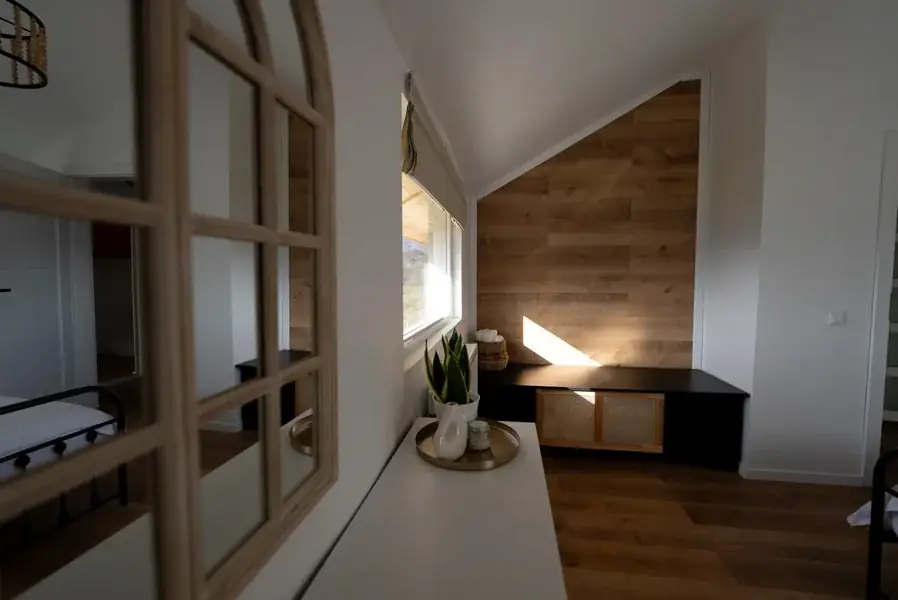 Corner of the queen bedroom under the eaves: a wood-clad wall, a window-frame mirror and plants