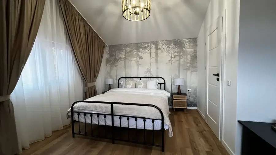 The queen bedroom: a black-framed double bed, misty-forest wallpaper and bedside lamps