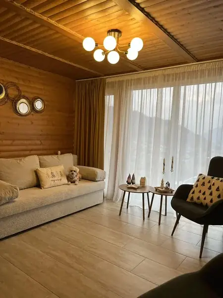 The living room with the lights on, the sofa bed and round side tables by the window