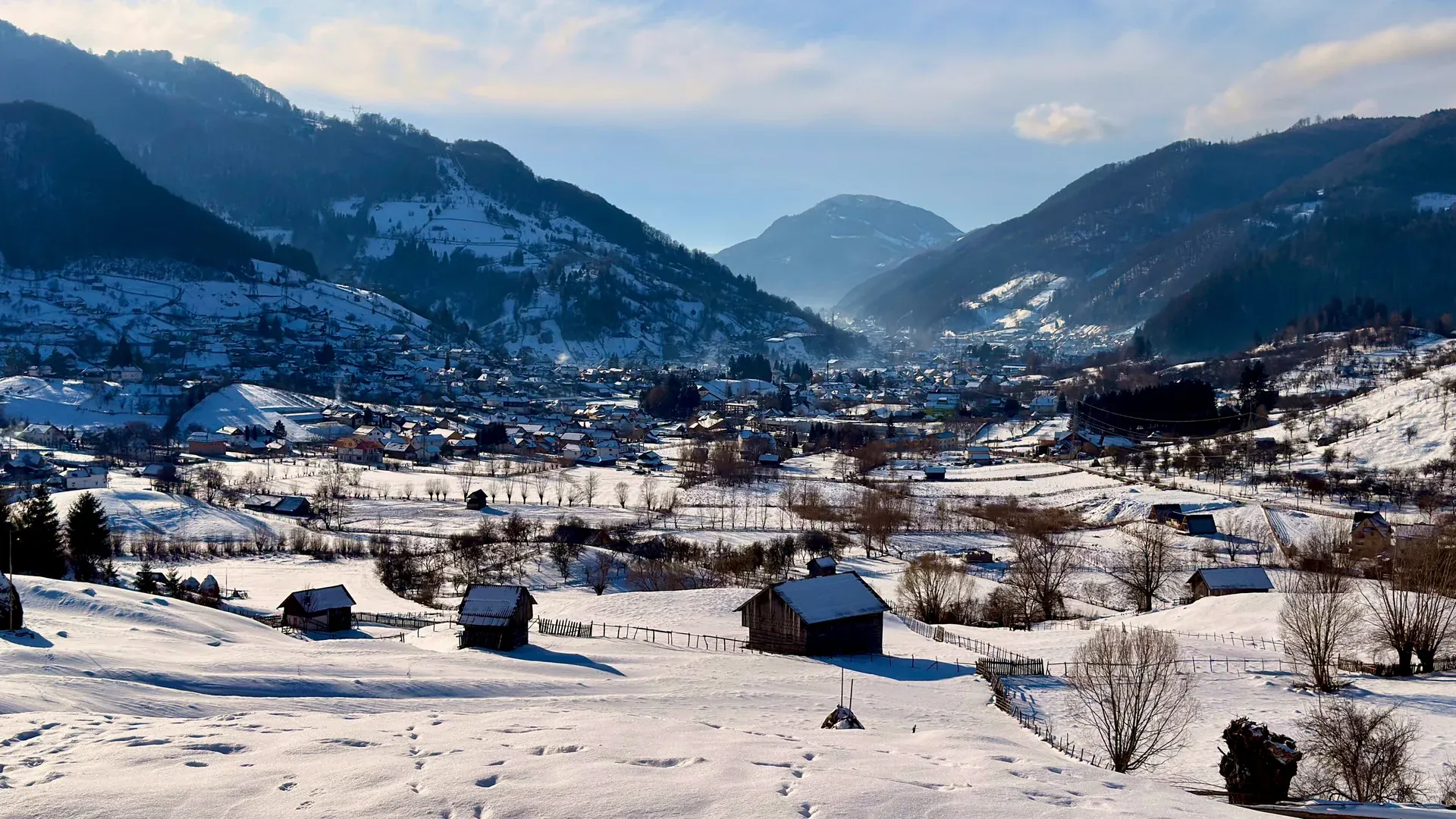 Winter on the hills: wooden barns under snow and the village in the valley