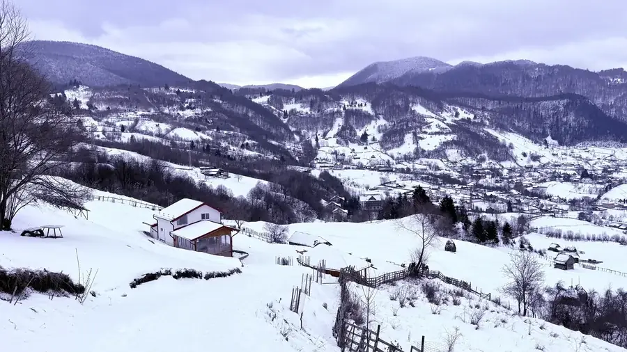 Winter in the Rucăr-Bran Corridor: a white house on the snowy hillside, mountains behind