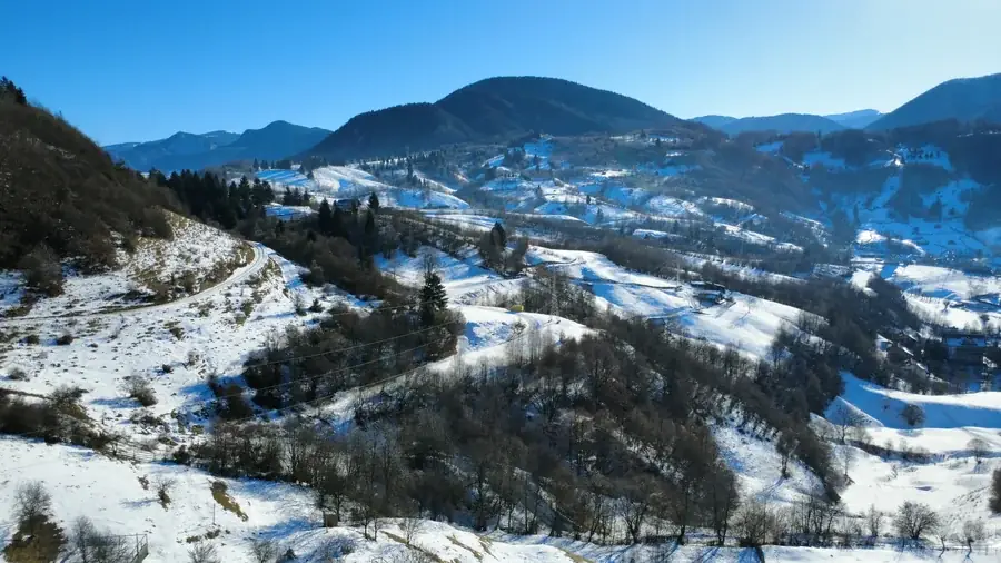 Drone view of snowy hills with patches of forest and scattered houses