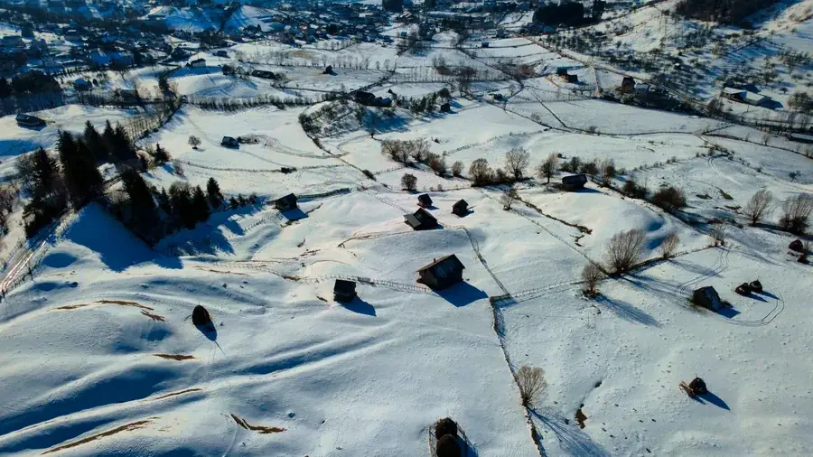 From above: snowy slopes with wooden barns and fences in low winter light
