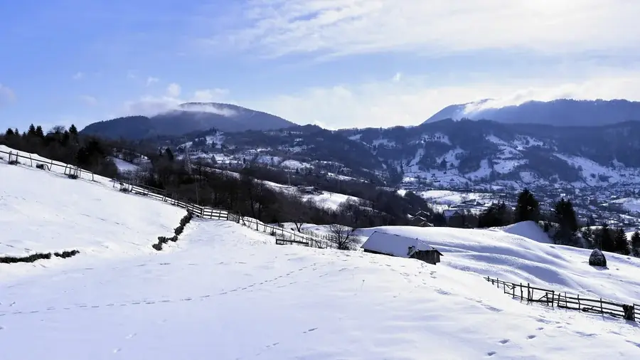 Deep snow on the meadows, wooden fences and white mountains under a blue sky