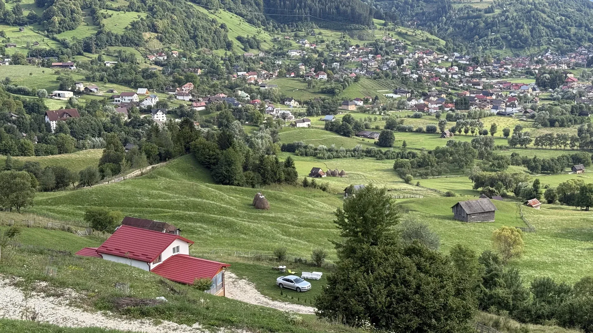 The white house with the red roof on the hillside, with Rucăr in the valley, in summer