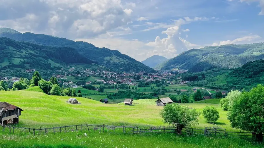 The garden in summer: green grass, a wooden fence and a view to the village and the mountains