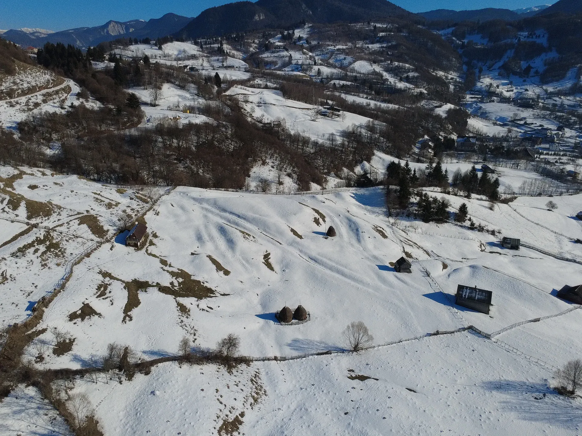 Winter from a drone: white slopes with a few barns and patches of forest